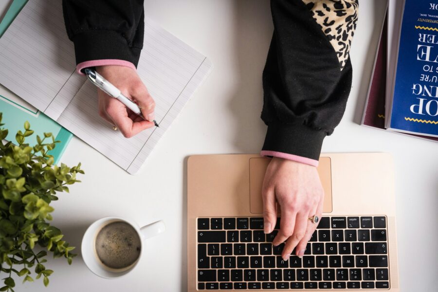 Person writing notebook laptop coffee